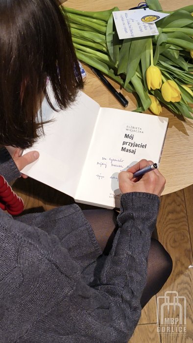 Biblioteka Gorlice, „Mój przyjaciel Masaj” — spotkanie autorskie z Elżbietą Wiejaczką Elżbieta Wiejaczka wpisuje dedykację do książki dla czytelników gorlickiej biblioteki