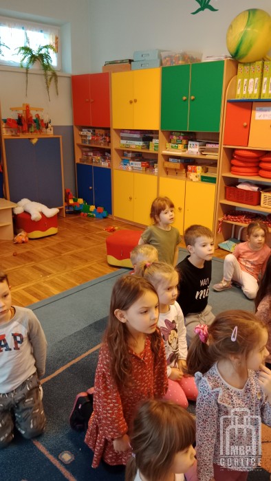 przedszkolaki klęczą słuchając jak bibliotekarka czyta