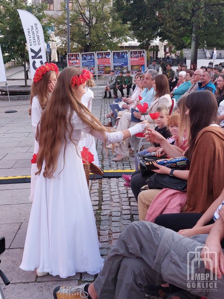 dziewczynki z gorlickich grup teatralnych rozdają kwiaty z bibuły zgromadzonej publiczności
